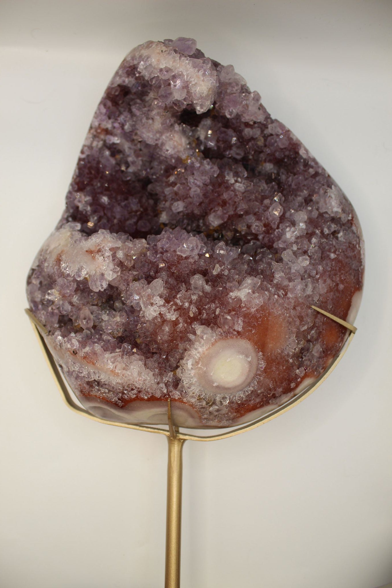 Close-up of a crystal formation with a white sphere inside, held by a gold stand against a neutral background.